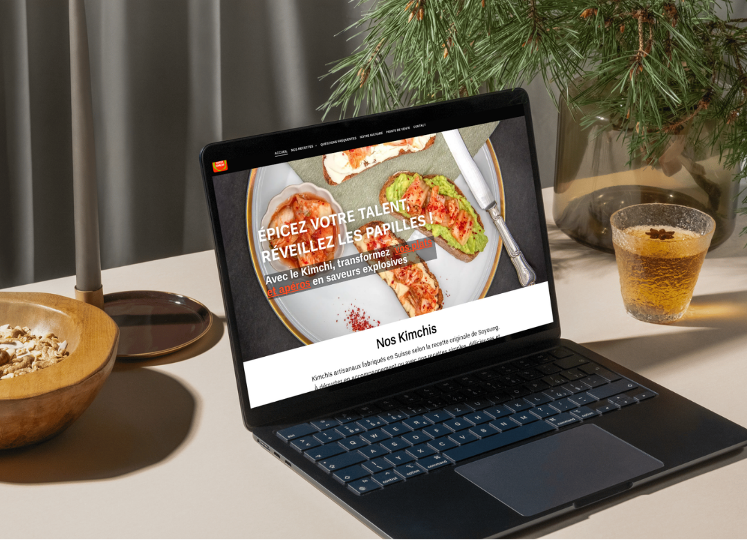 Un ordinateur portable affichant un site web culinaire, à côté d'une boisson et d'un bol, avec un brin de verdure en arrière-plan.
