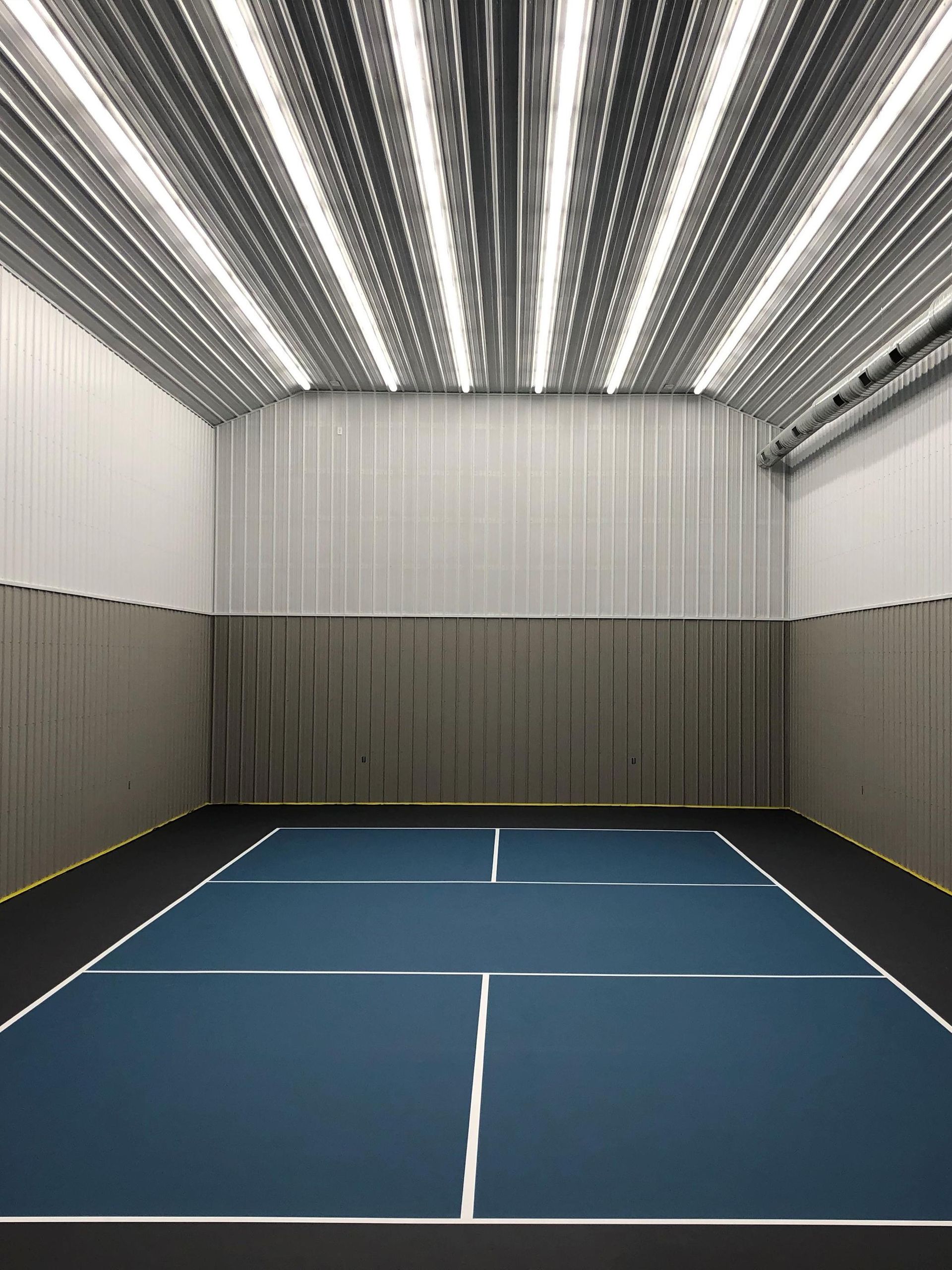 Indoor pickleball court with blue playing surface and white lines, surrounded by padded walls.