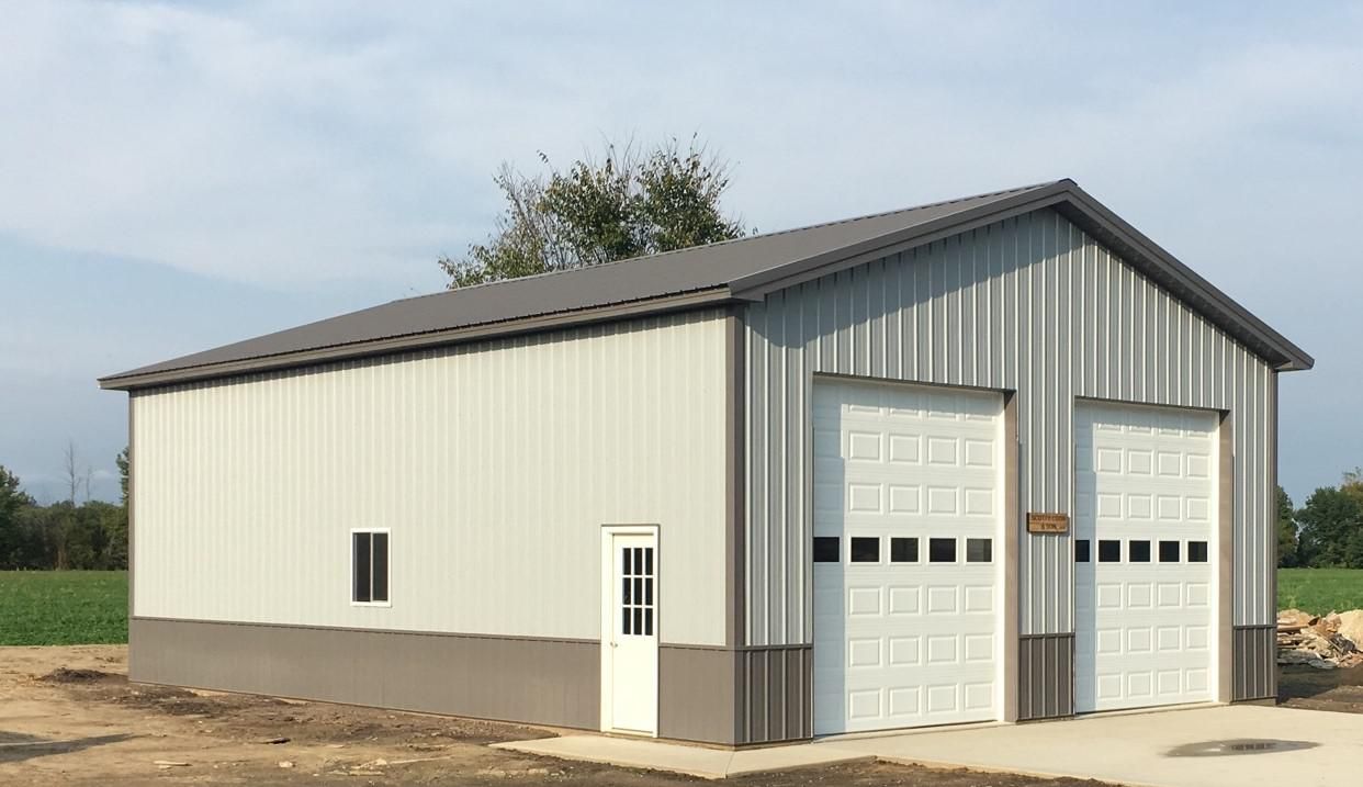 Two-bay metal garage with gray roof, white doors, and a small side window; set outdoors on a concrete pad.