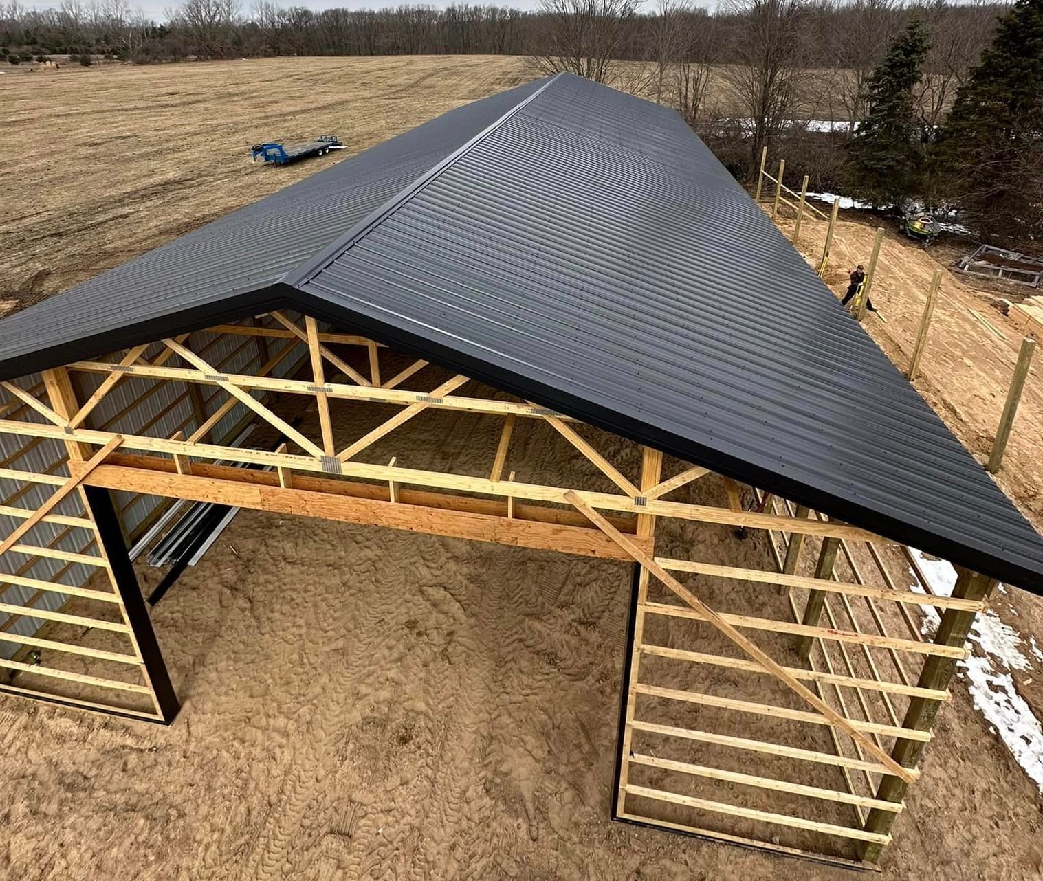 Unfinished barn with a dark metal roof, wood framing, and open entrances; outdoor setting.