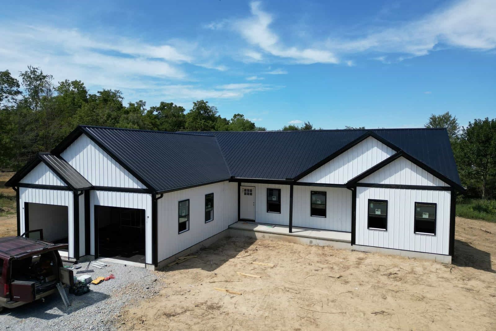 White house with black trim and roof, under construction. Garage and porch. Blue sky.