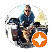 Man in blue hoodie, sunglasses, sits in truck bed with deer head, orange star logo in corner.