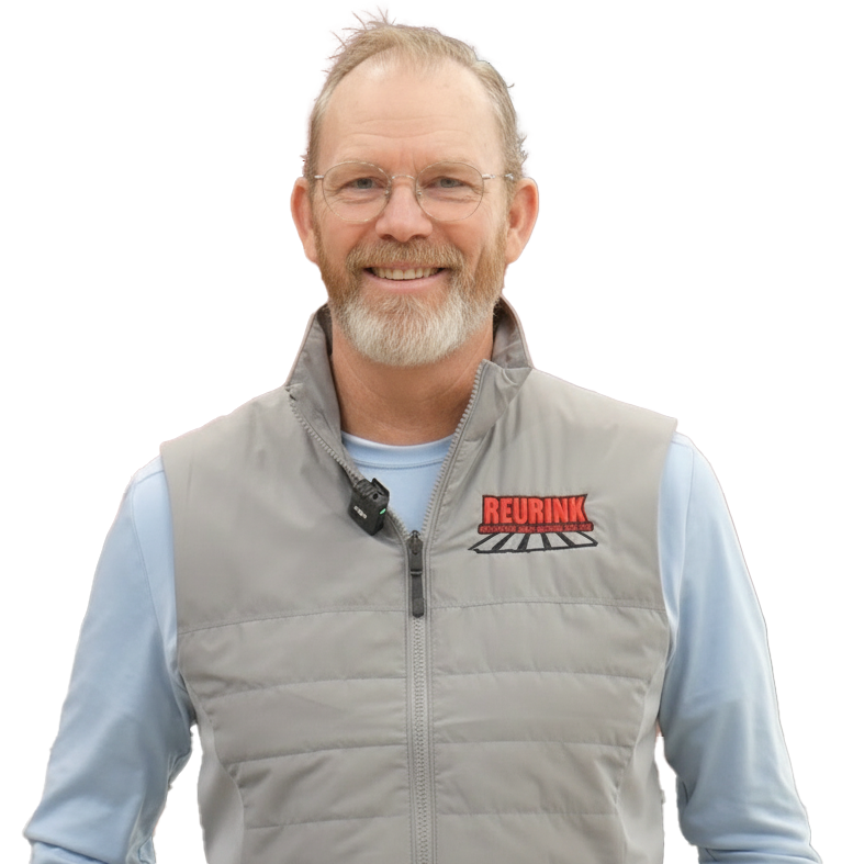Man wearing a gray vest with a logo over a light blue long-sleeved shirt, smiling.