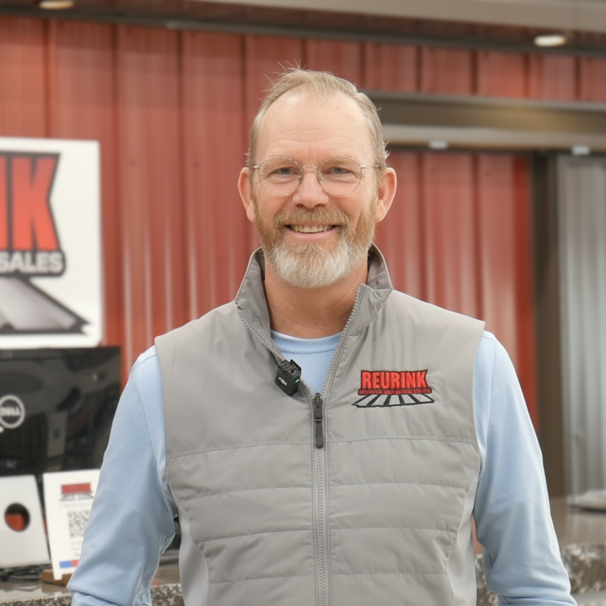 Man with beard in gray vest, in front of a sign that says