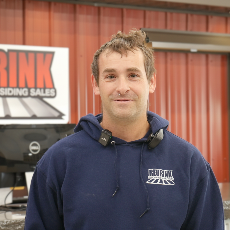 Man in a blue hoodie, standing in front of a red building with a company sign.