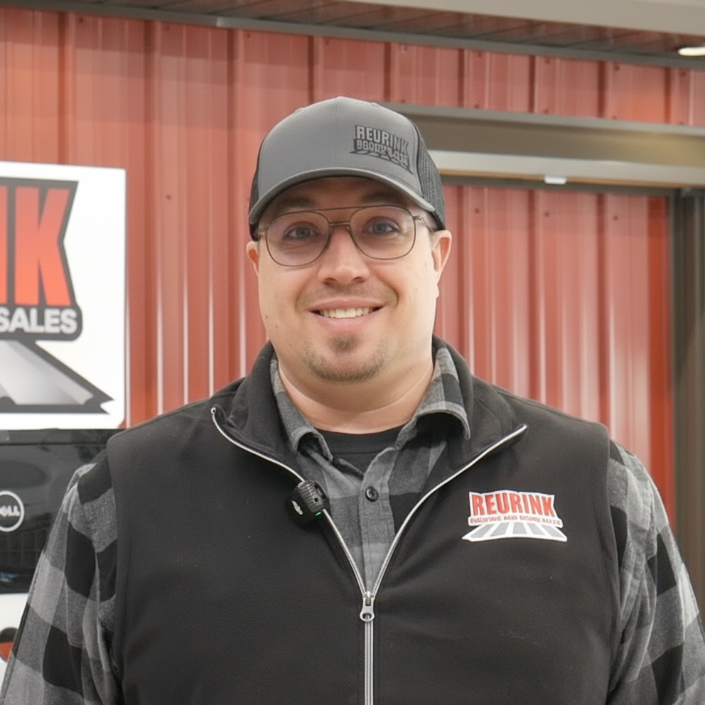 Man wearing a hat and glasses smiling. He's standing in front of a building with a Redrink sign.