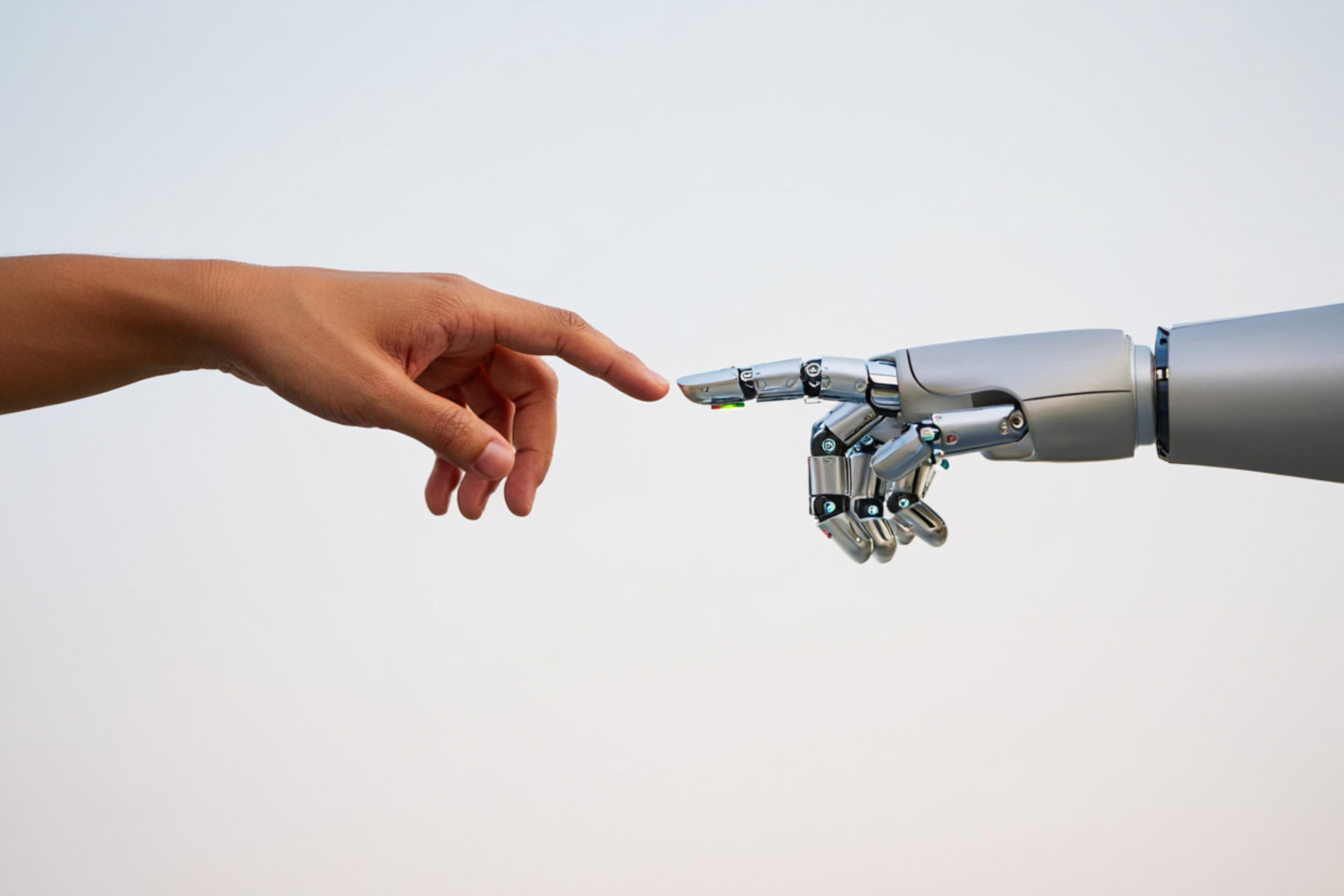 Human hand touching a robot hand, a modern take on the Sistine Chapel's creation scene, against a light background.
