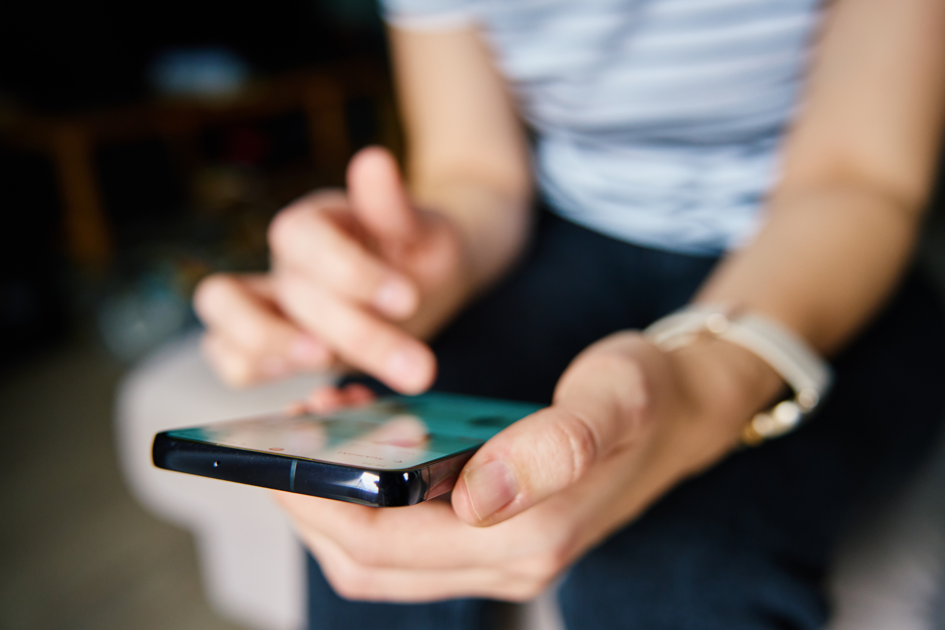 Person using a smartphone, focusing on the screen. They are indoors, with hands and a watch visible.