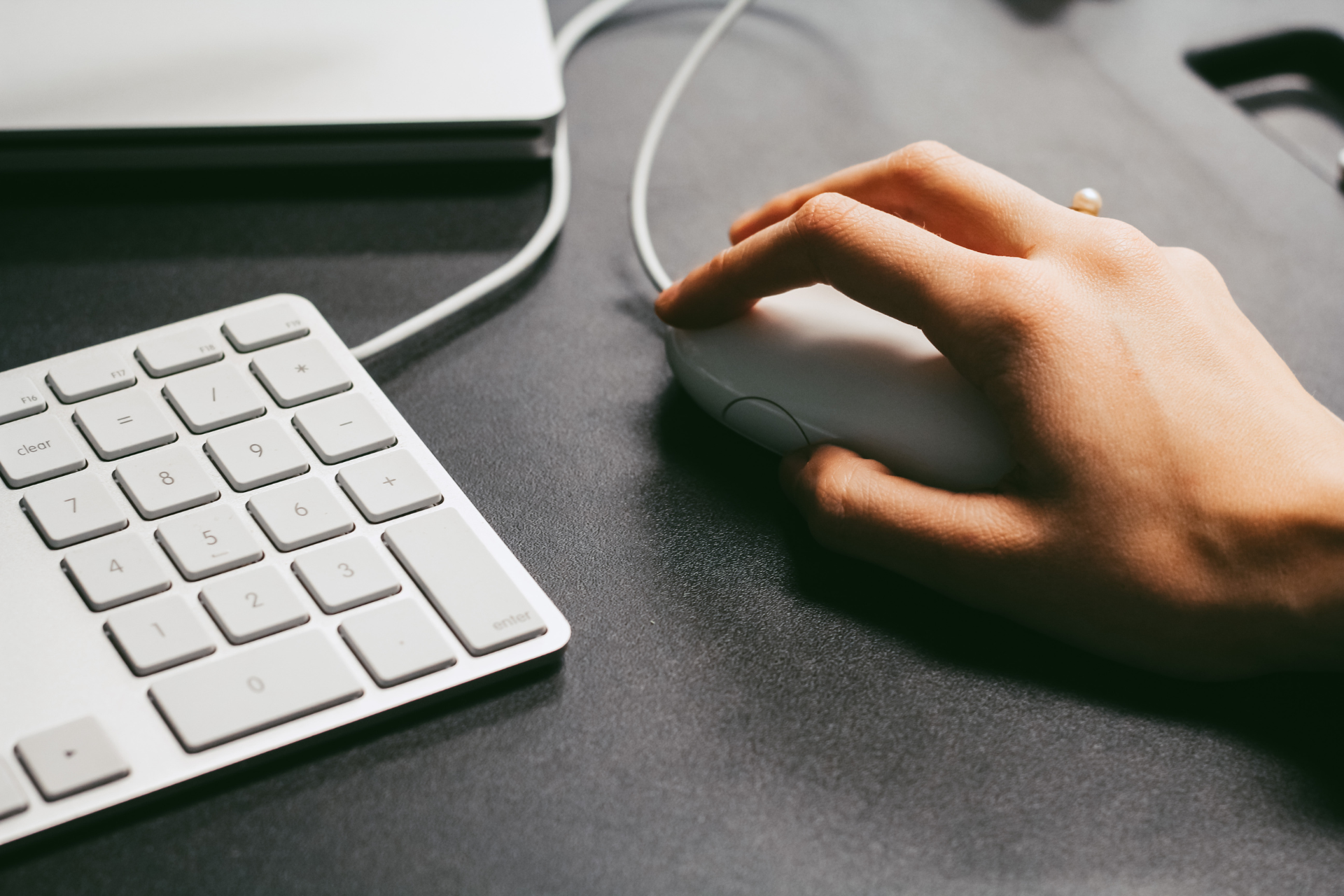 Hand using a white computer mouse next to a white keyboard on a dark desk.