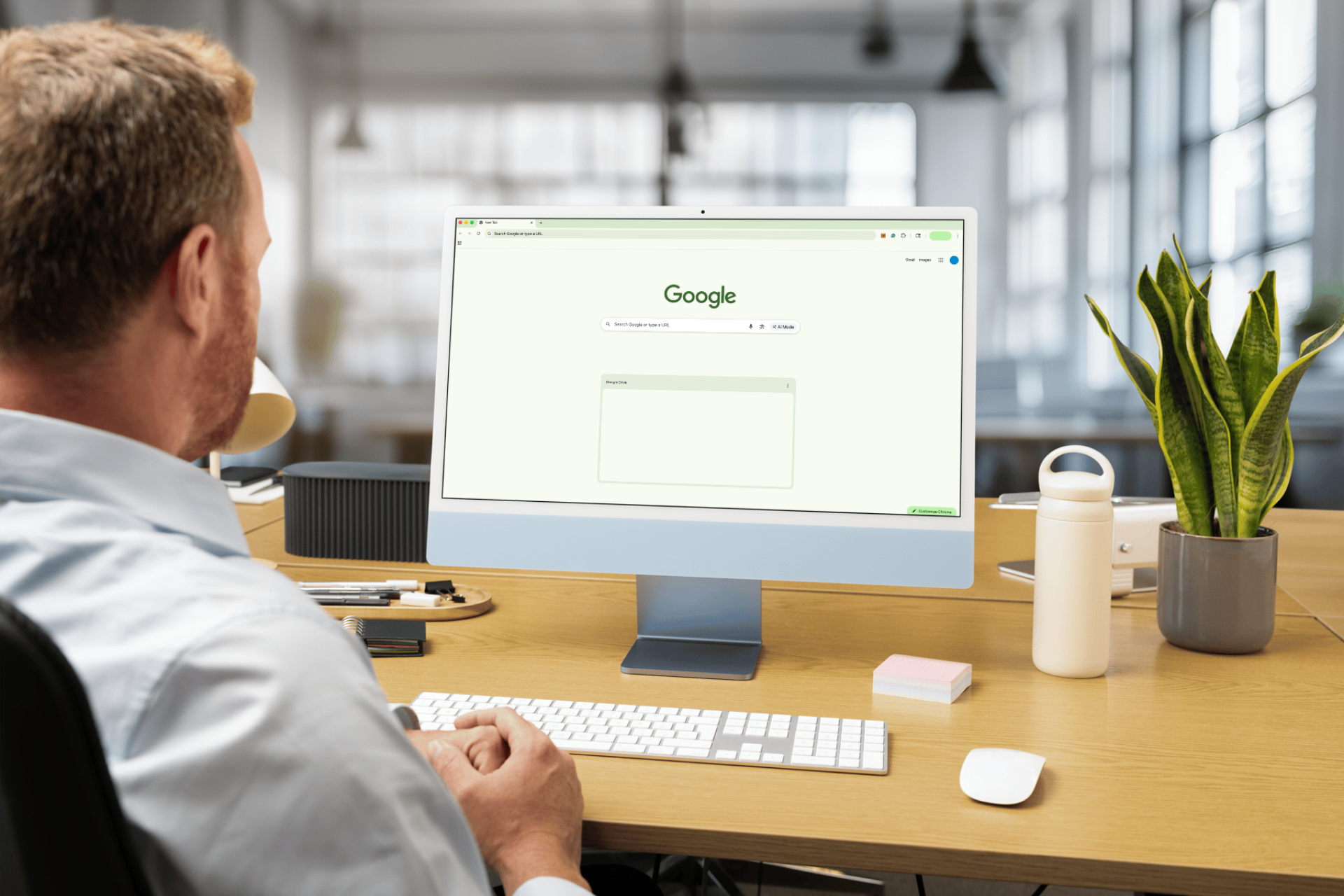 Man using a desktop computer with a Google search bar open. Light-filled office with a plant.