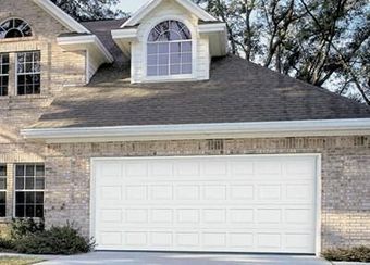 White garage door on a two-story brick house with windows, beneath a dark roof and a dormer window.