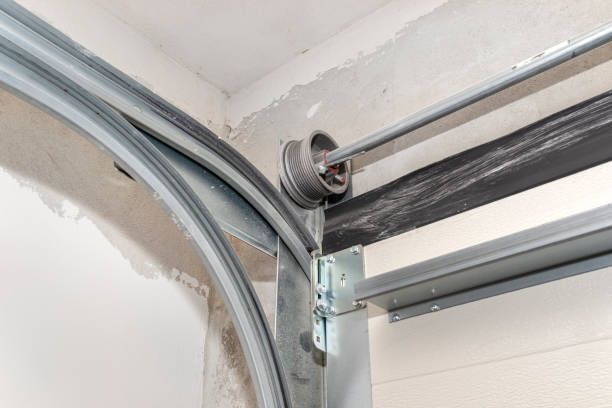 Garage door track with a roller at the curve, attached to a metal frame within a white garage.
