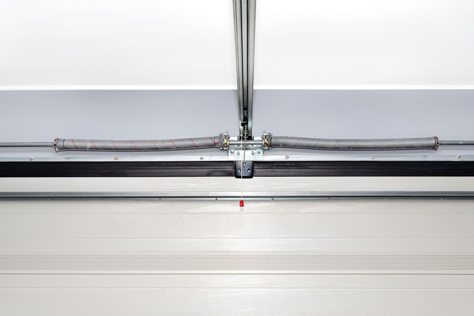 Garage door spring assembly, horizontal with silver hardware, mounted above a closed white door.