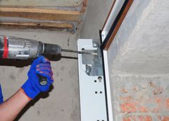 Person wearing blue gloves using a drill to install a garage door mechanism.