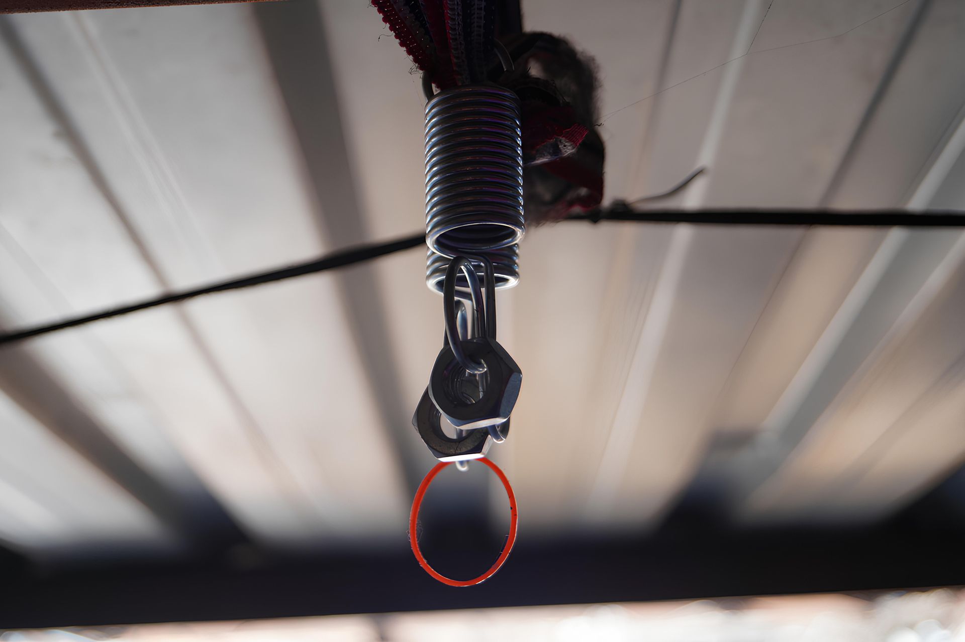 Black sprinkler head hanging from a corrugated metal ceiling with an orange loop attached.