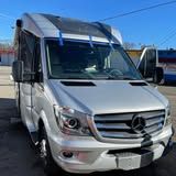 A silver mercedes benz sprinter van is parked in a parking lot.