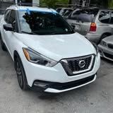 A white nissan kicks is parked in a lot.