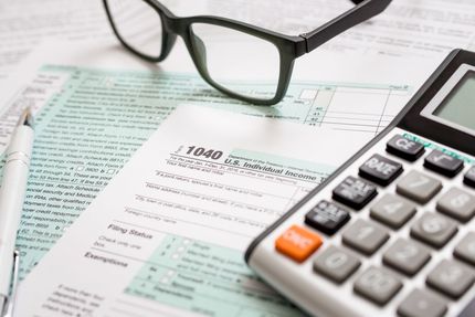 A pair of glasses and a calculator are sitting on top of a tax form.