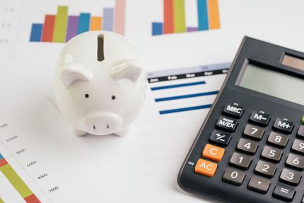 A piggy bank is sitting next to a calculator on a table.