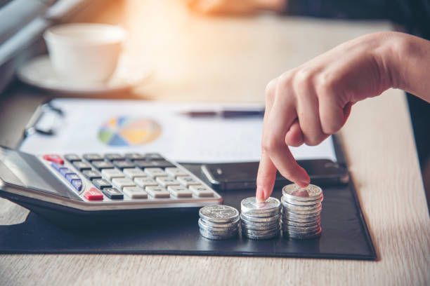 A person is stacking coins on a desk in front of a calculator.