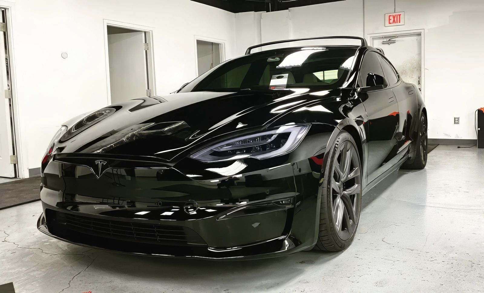 Black Tesla Model S car parked in a garage, with tinted windows and black wheels.