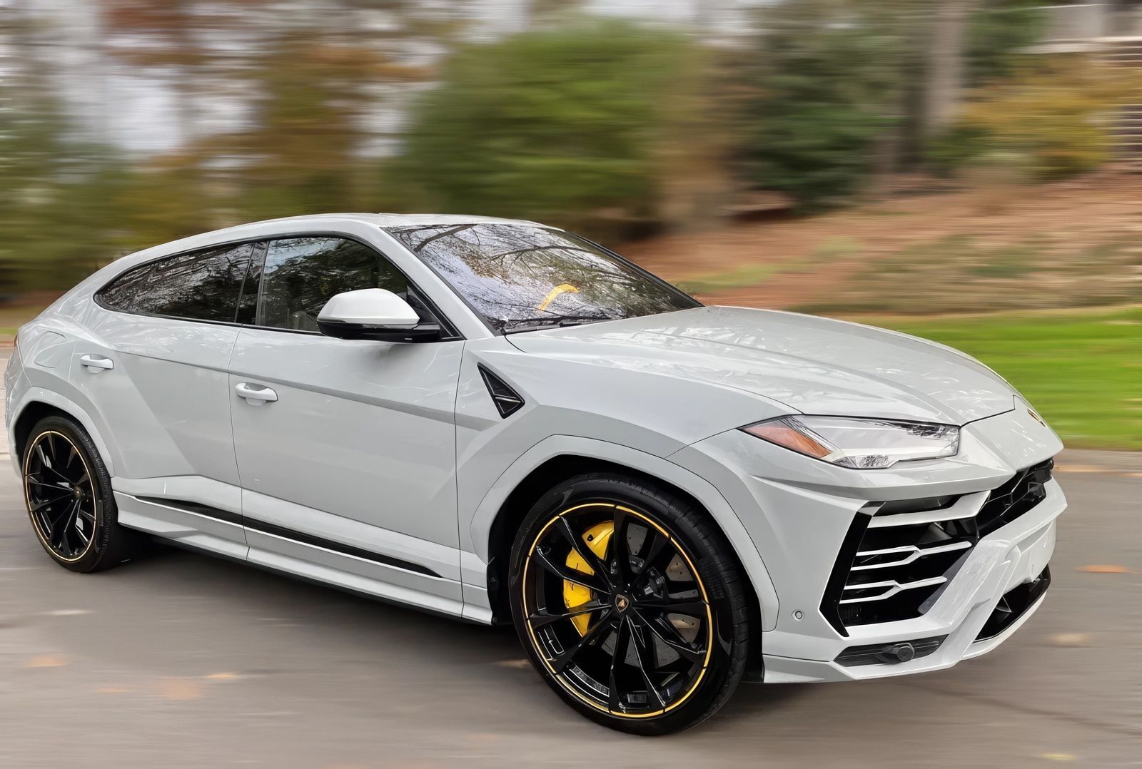 Gray Lamborghini Urus SUV with black and yellow wheels driving on a road.