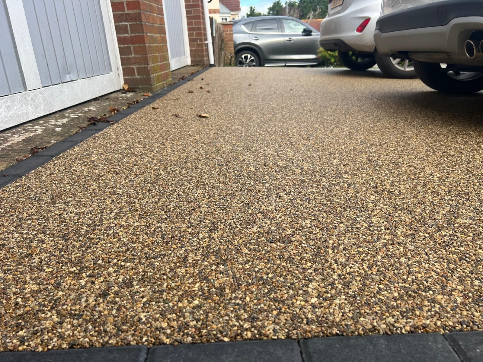A car is parked on a gravel driveway next to a garage.