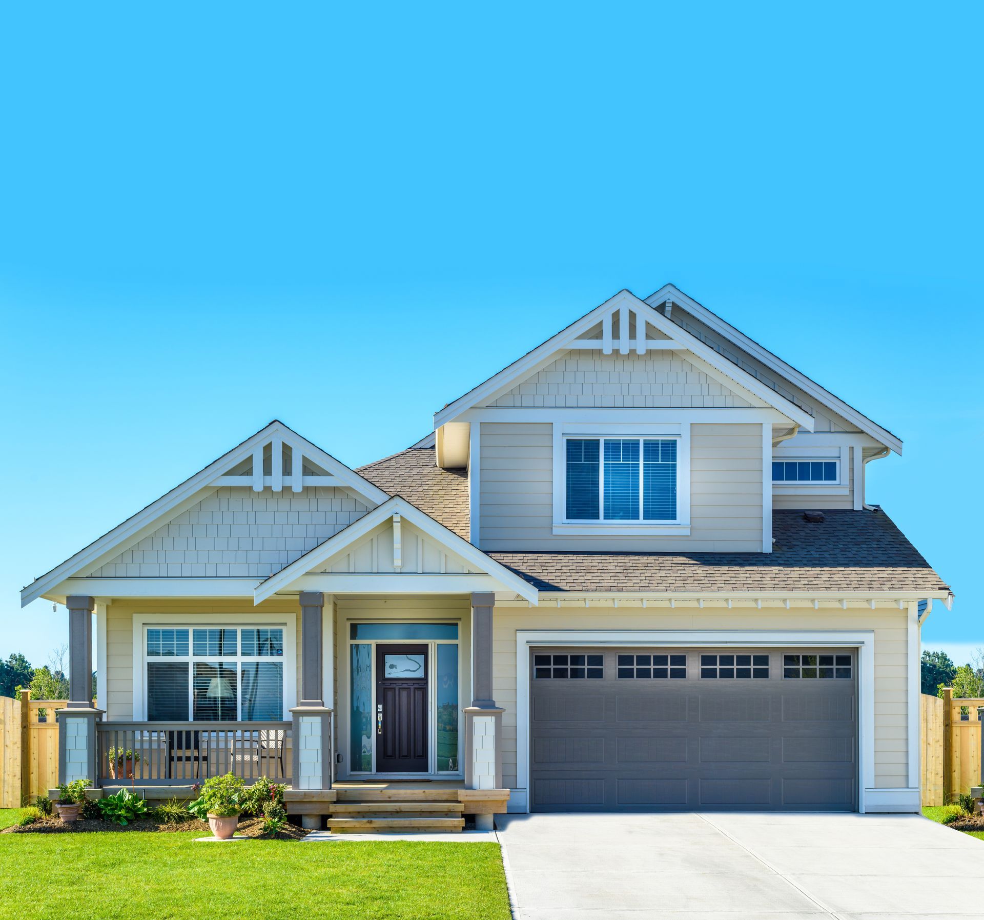 Suburban two-story house with gray siding, front porch, garage, and green lawn under a blue sky