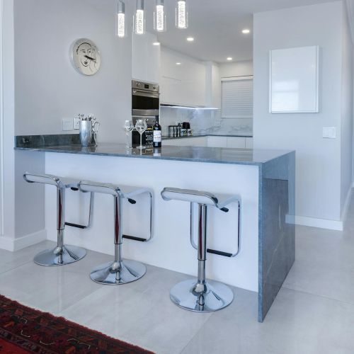 A kitchen with three bar stools and a clock on the wall