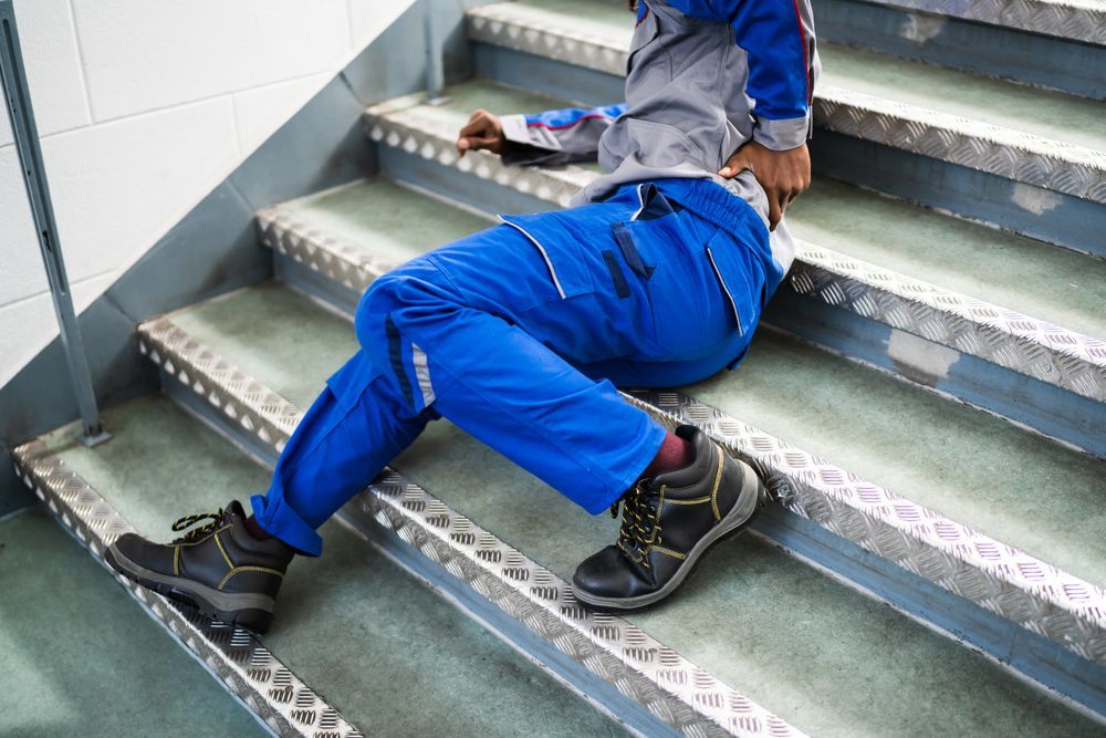 Person wearing blue work clothes on metal stairs, appears to have fallen.