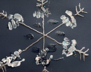 A six point child-made snowflake created with glitter glue and inward-pointing chevrons on the ends on black construction paper. The spines are decorated with handprints in white ink.