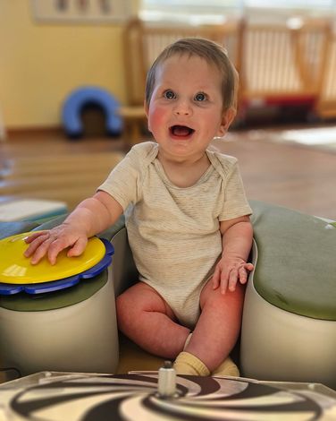 Child smiling at camera while sitting in wheelchair with tray and toy.