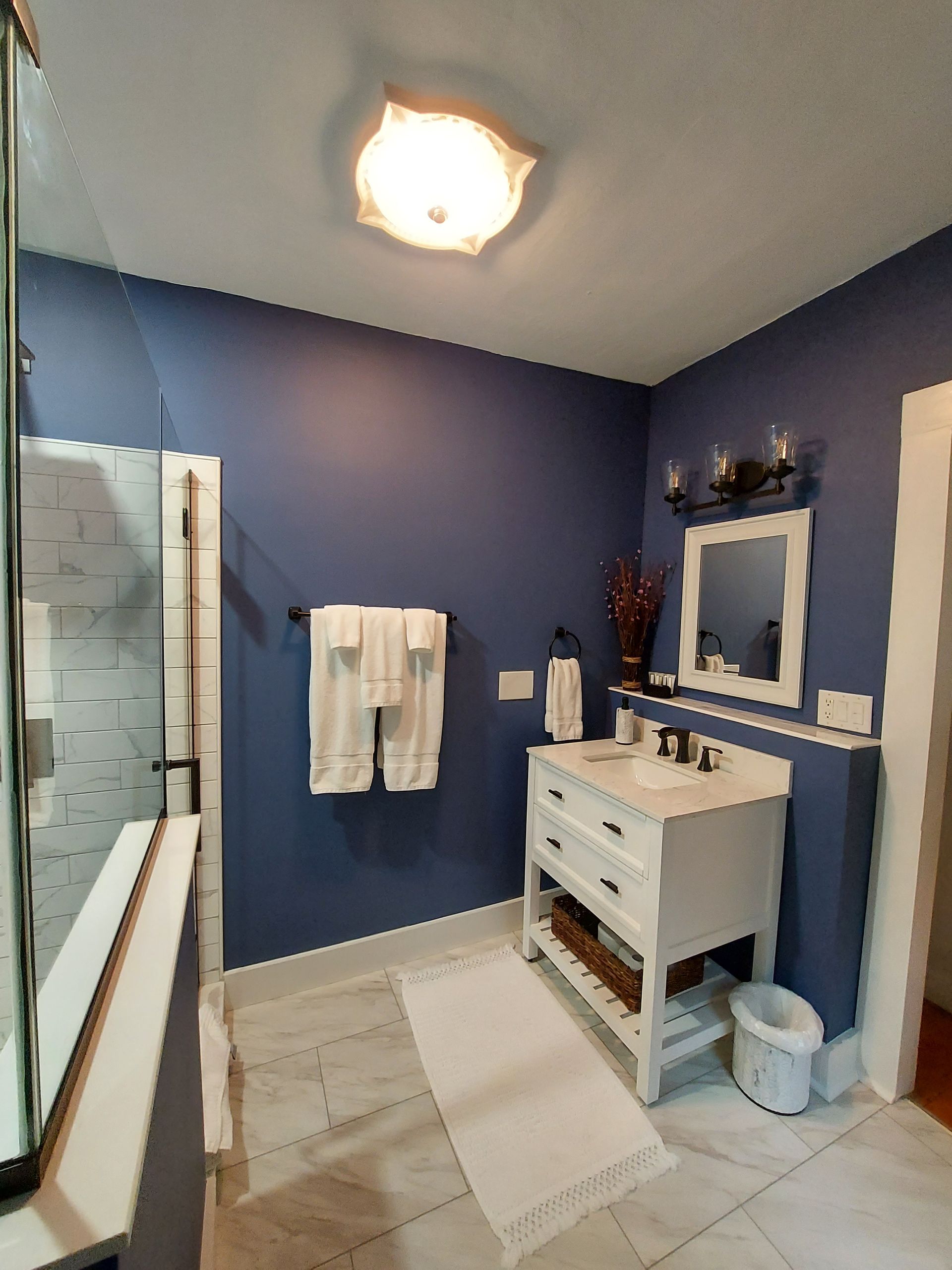 a bathroom with blue walls , a white vanity , a mirror and a walk in shower .