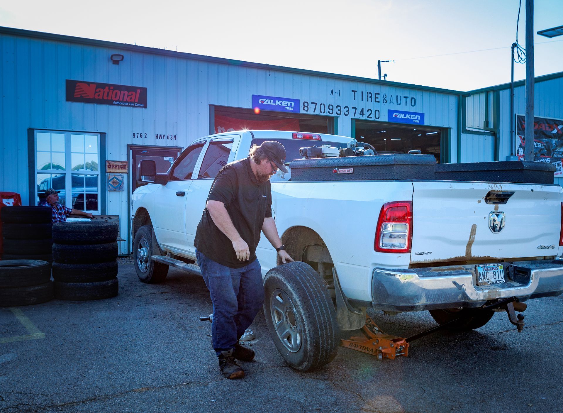 Mechanic changing a tire on a white pickup truck outside a tire shop.