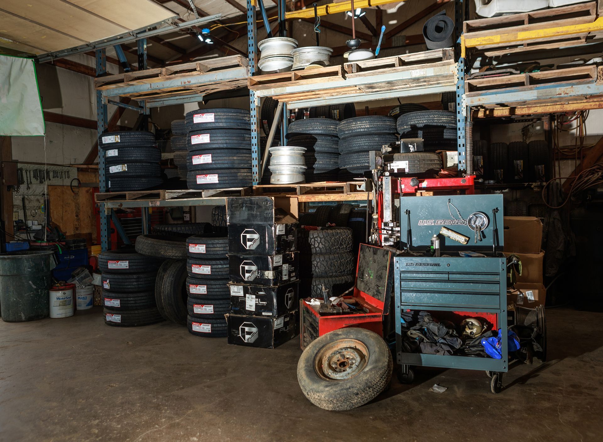 Tire shop interior with stacked tires, equipment, and shelves filled with wheels and tools.