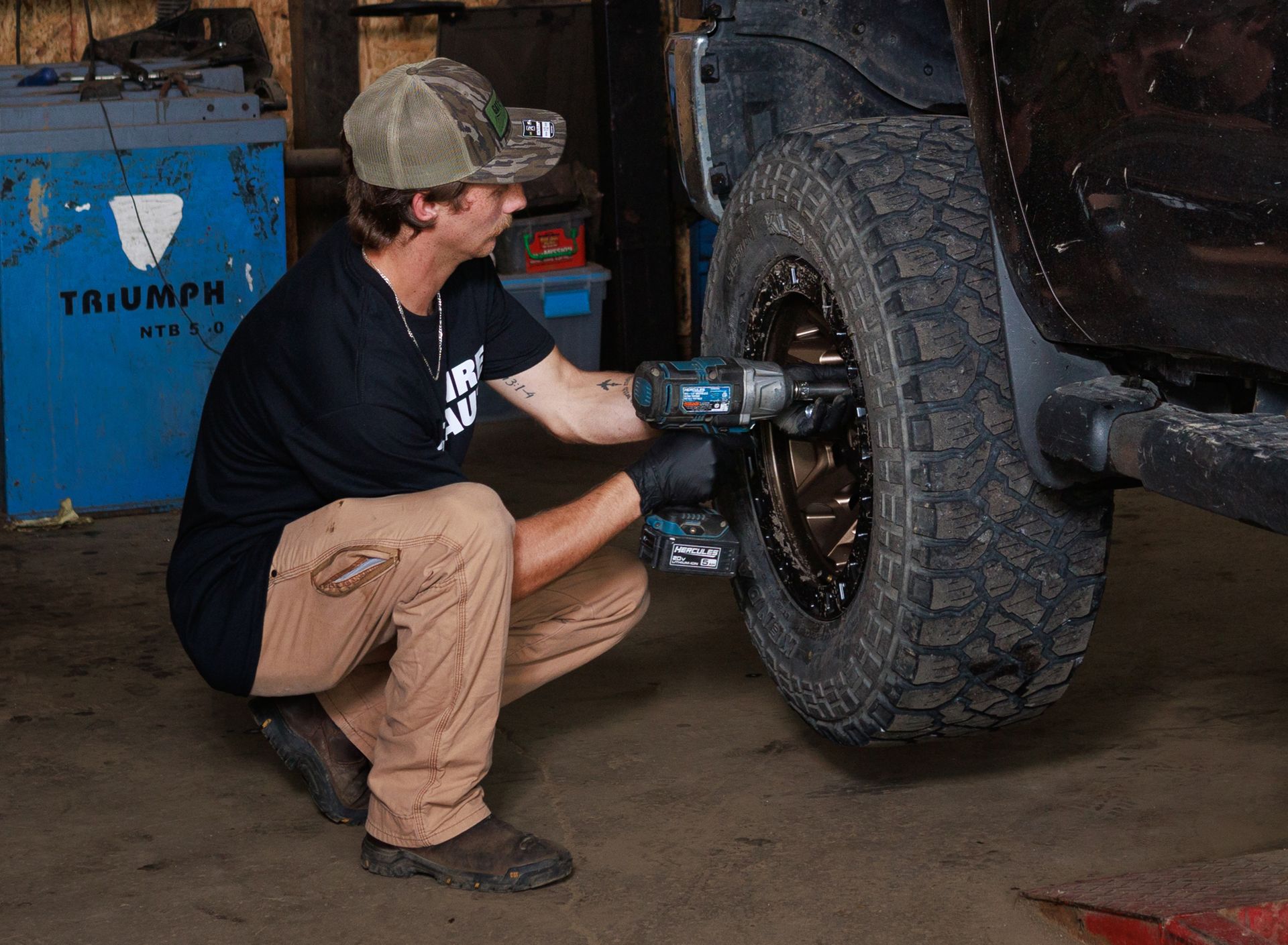 Mechanic using power tool to remove lug nuts from a vehicle's tire in a garage.