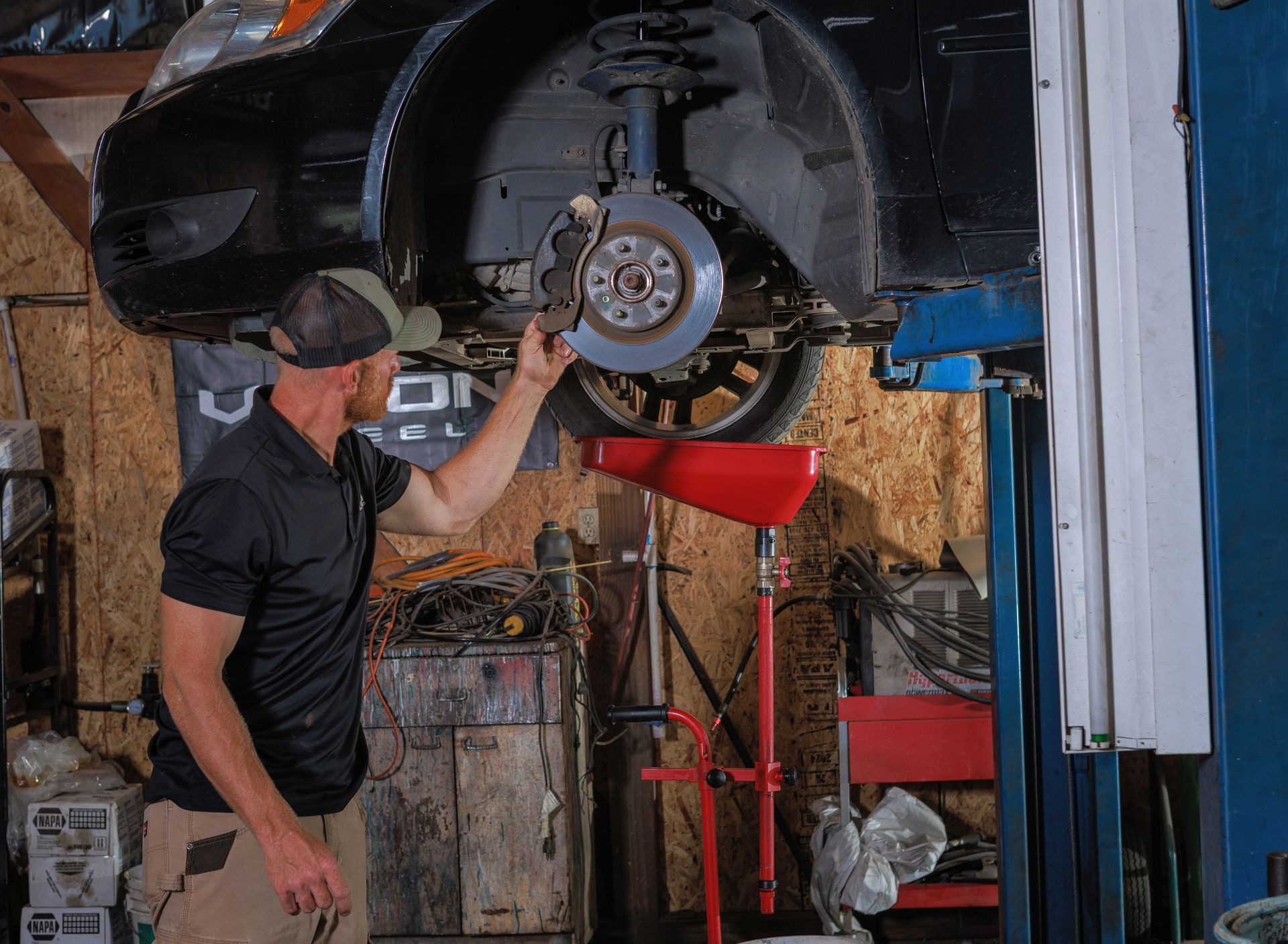 Mechanic examining a car's brake disc while the vehicle is lifted in a workshop.