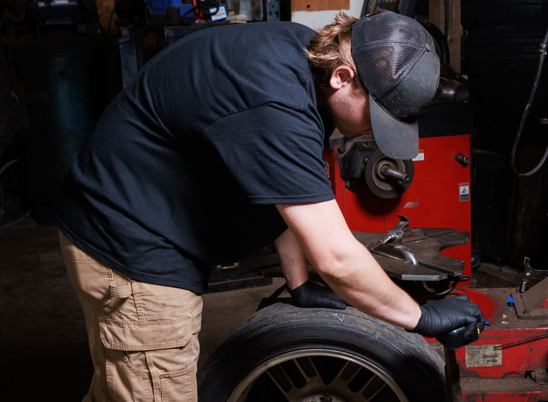 Mechanic in black shirt and cap working on a tire in a garage.