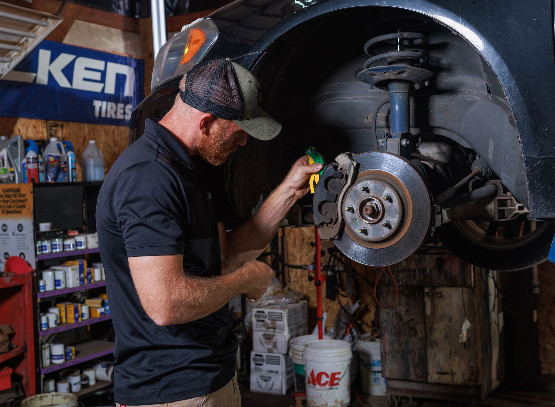 Mechanic working on car brakes in a garage, using a tool. Brake rotor and caliper visible.