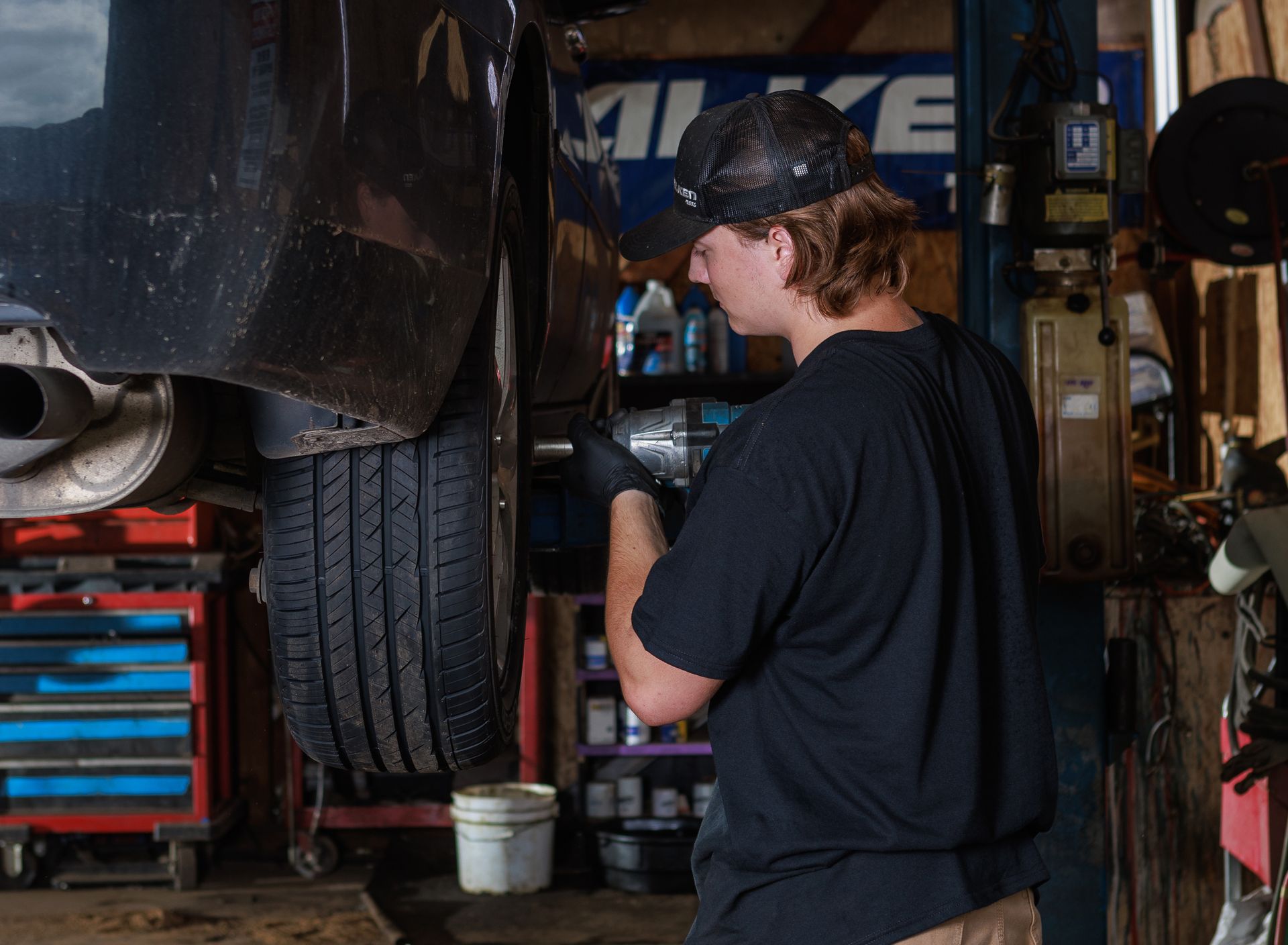 Mechanic using a power tool on a car tire in a garage.