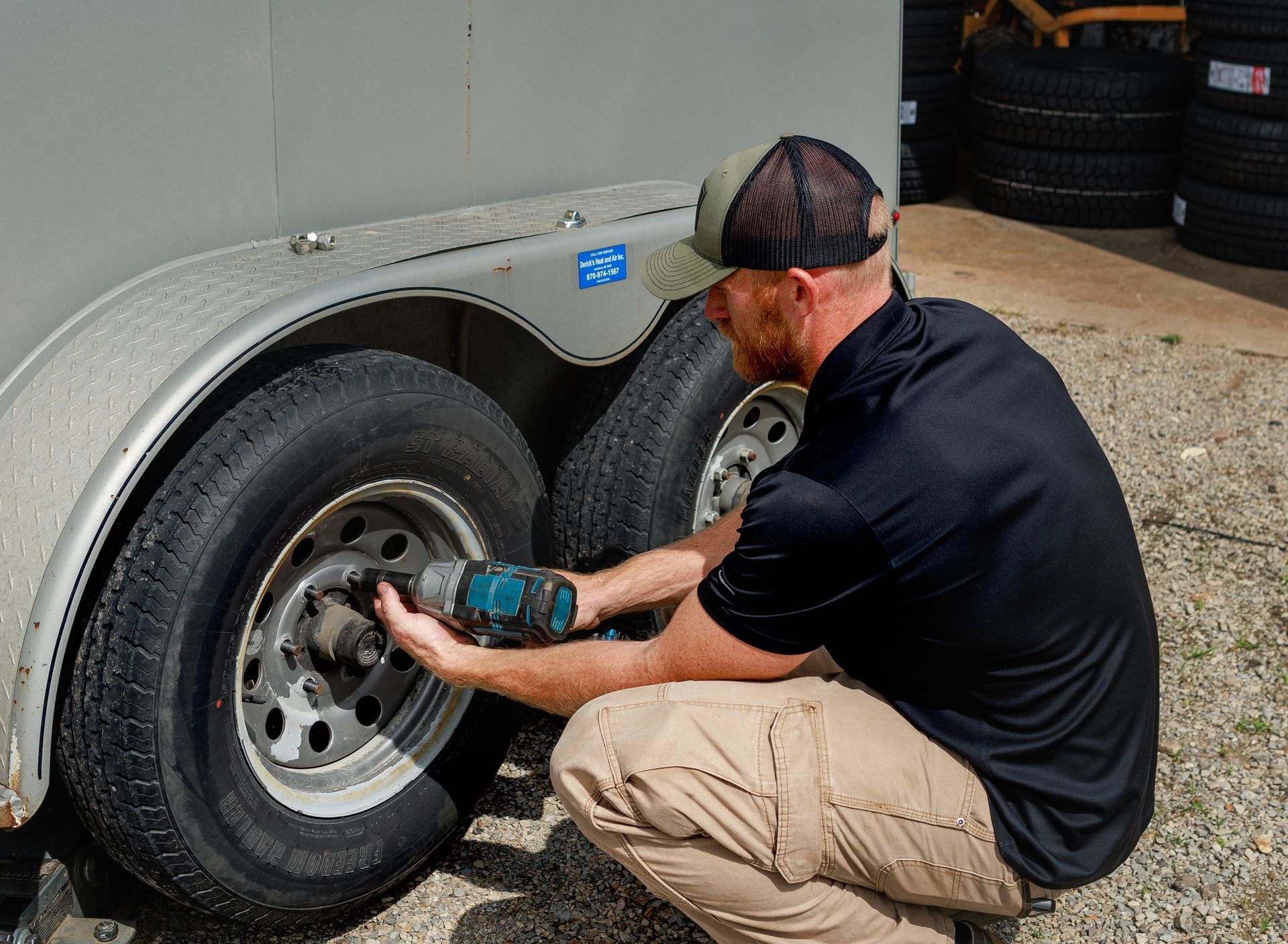 Man uses power tool to work on trailer tire.
