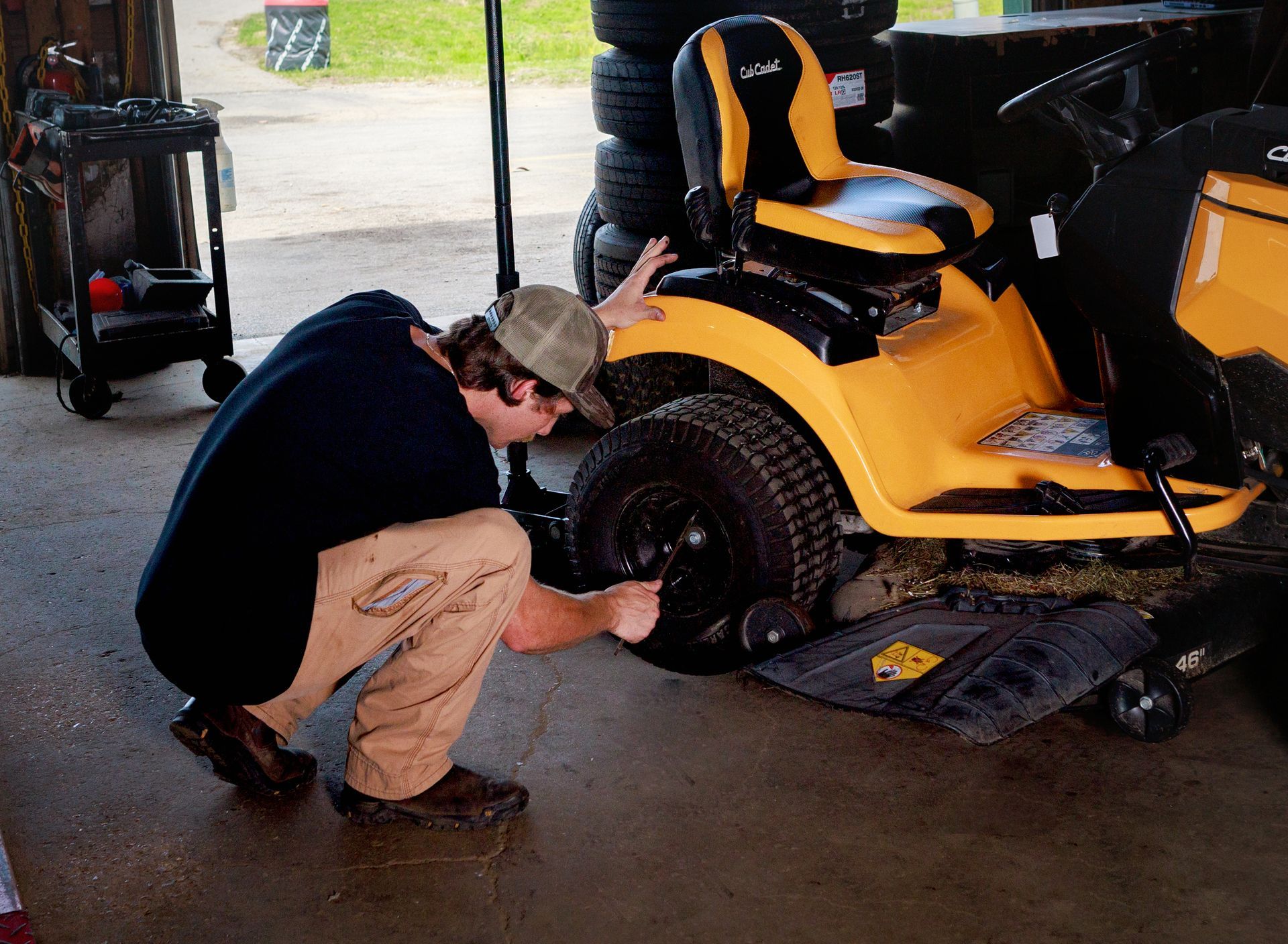 Person working on the front wheel of a yellow lawn tractor in a garage.