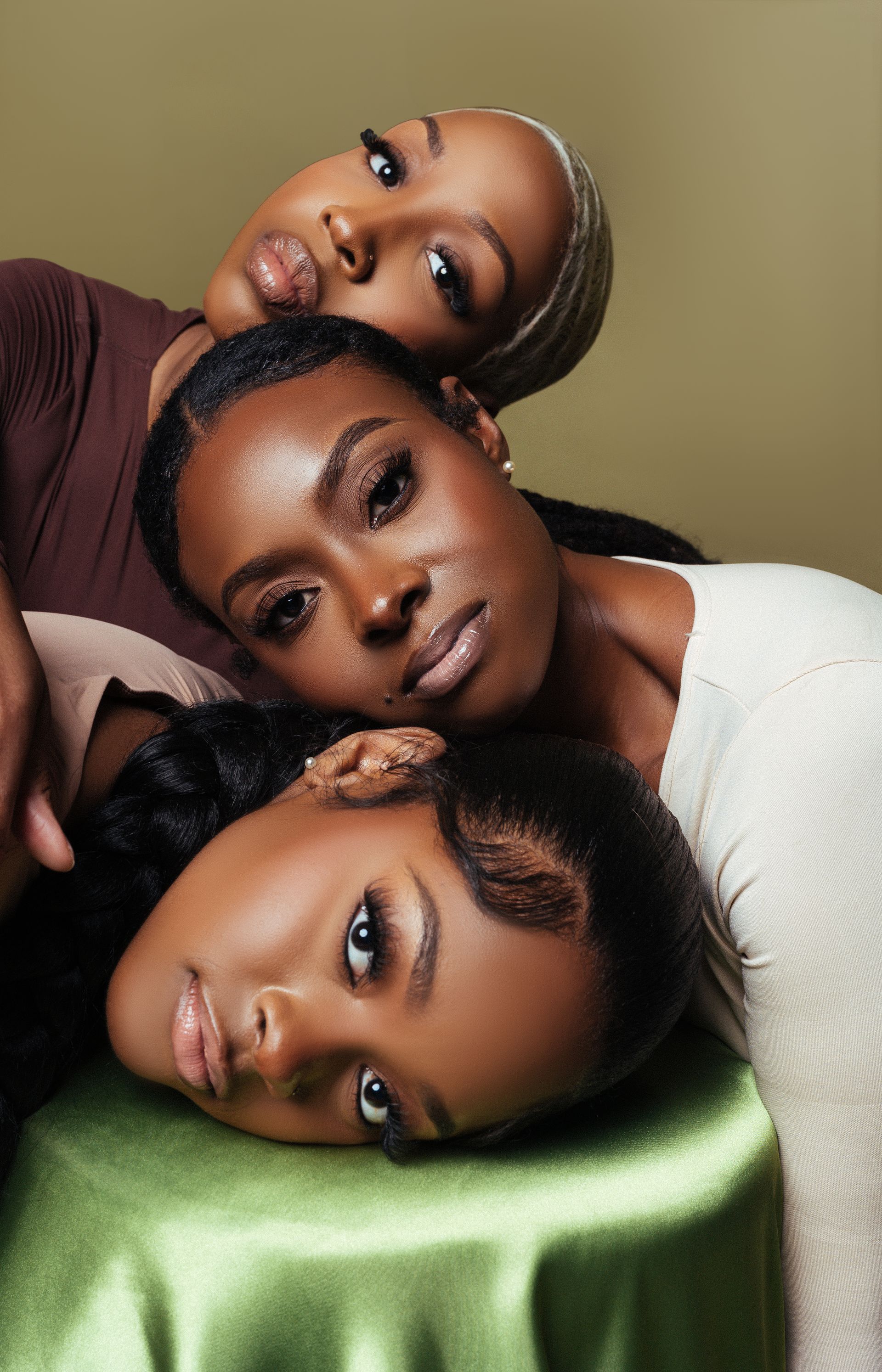 Three women are laying on top of each other on a green table cloth.