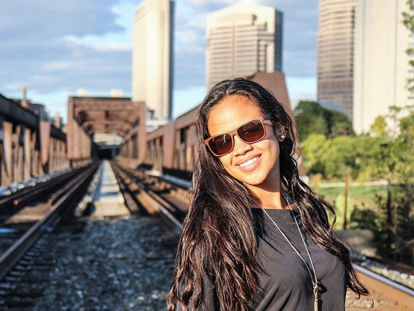 A woman wearing sunglasses is standing on train tracks.