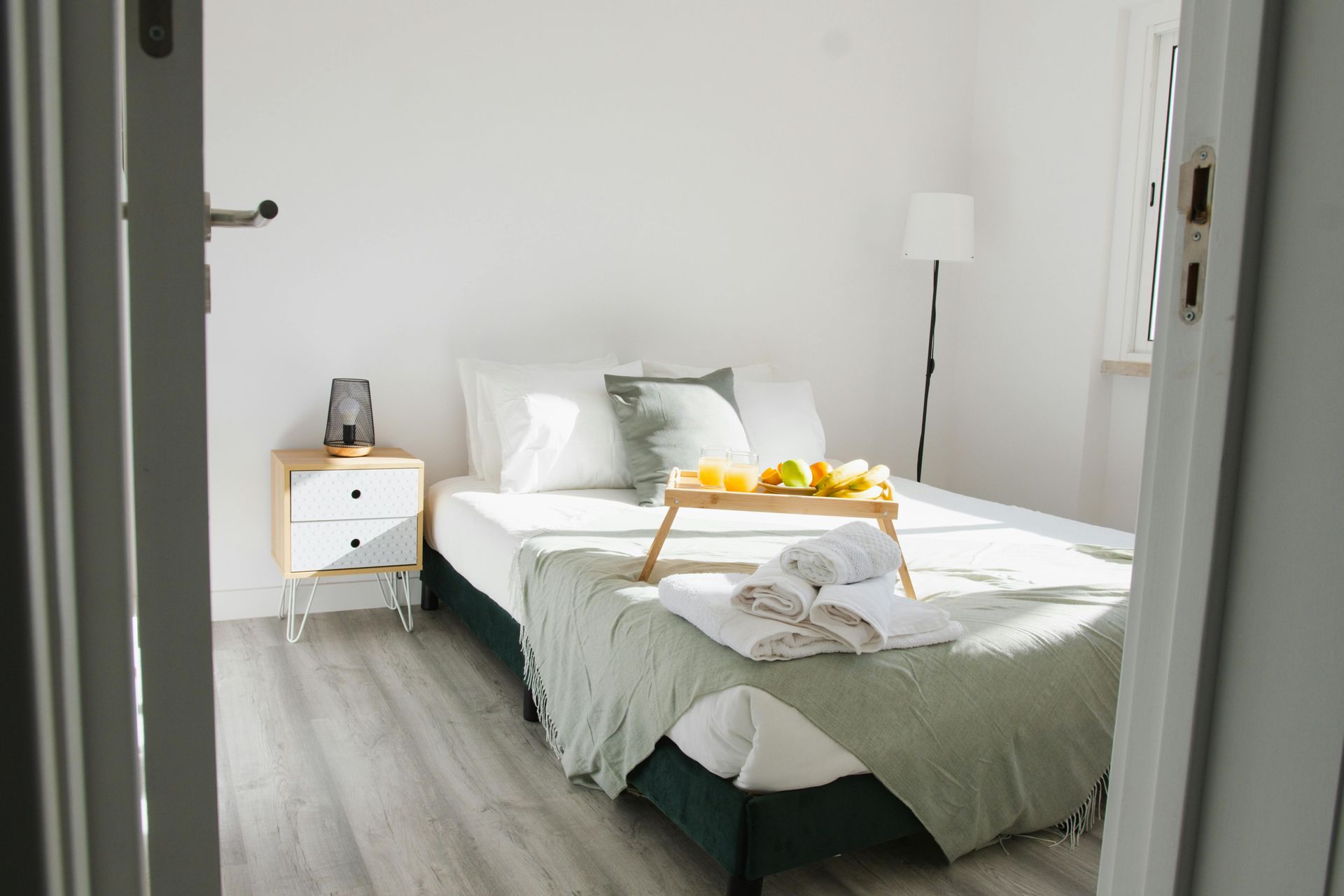 Bedroom with bed, tray of food, and nightstand, seen through a doorway.