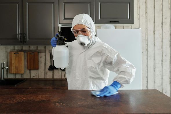 Person in hazmat suit spraying and wiping a kitchen countertop.