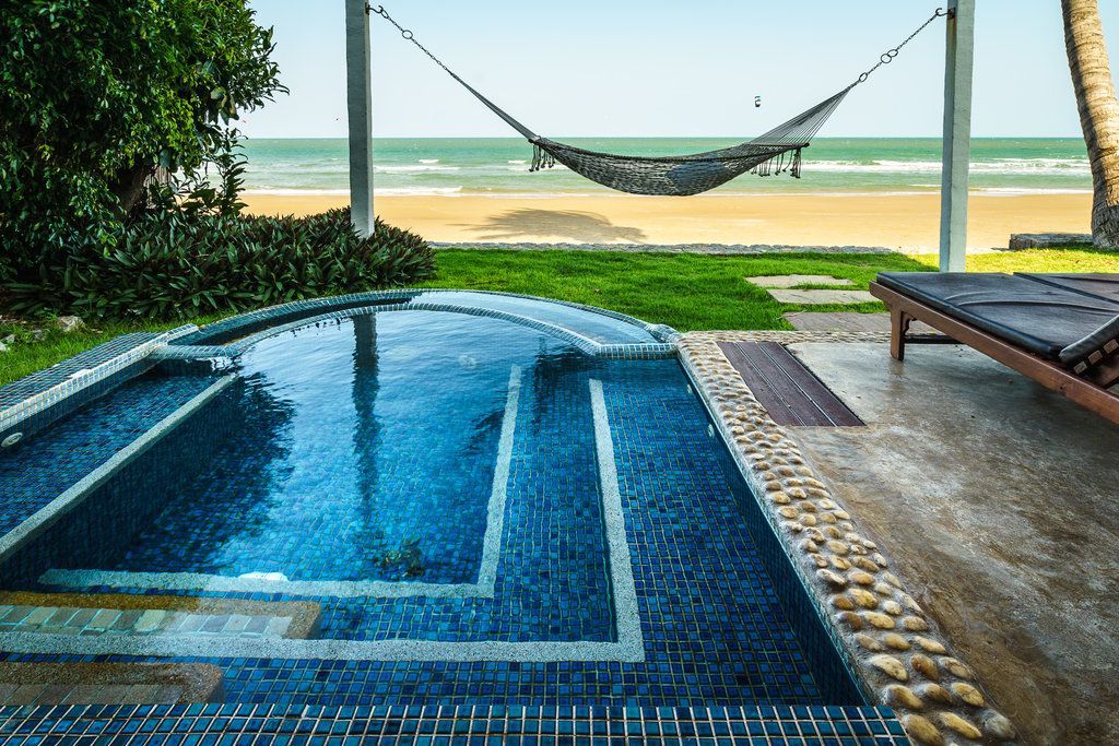 A swimming pool with a hammock hanging over it and a beach in the background.