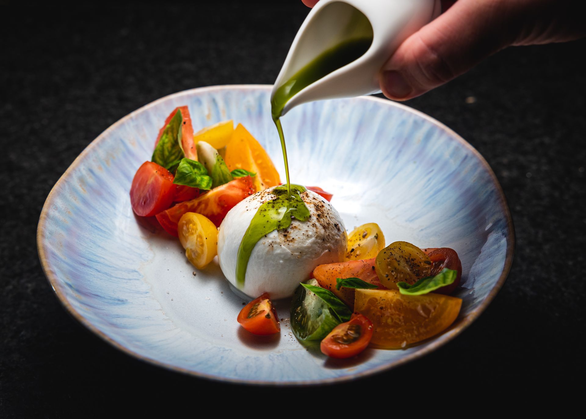 A person is pouring green sauce on a plate of food.