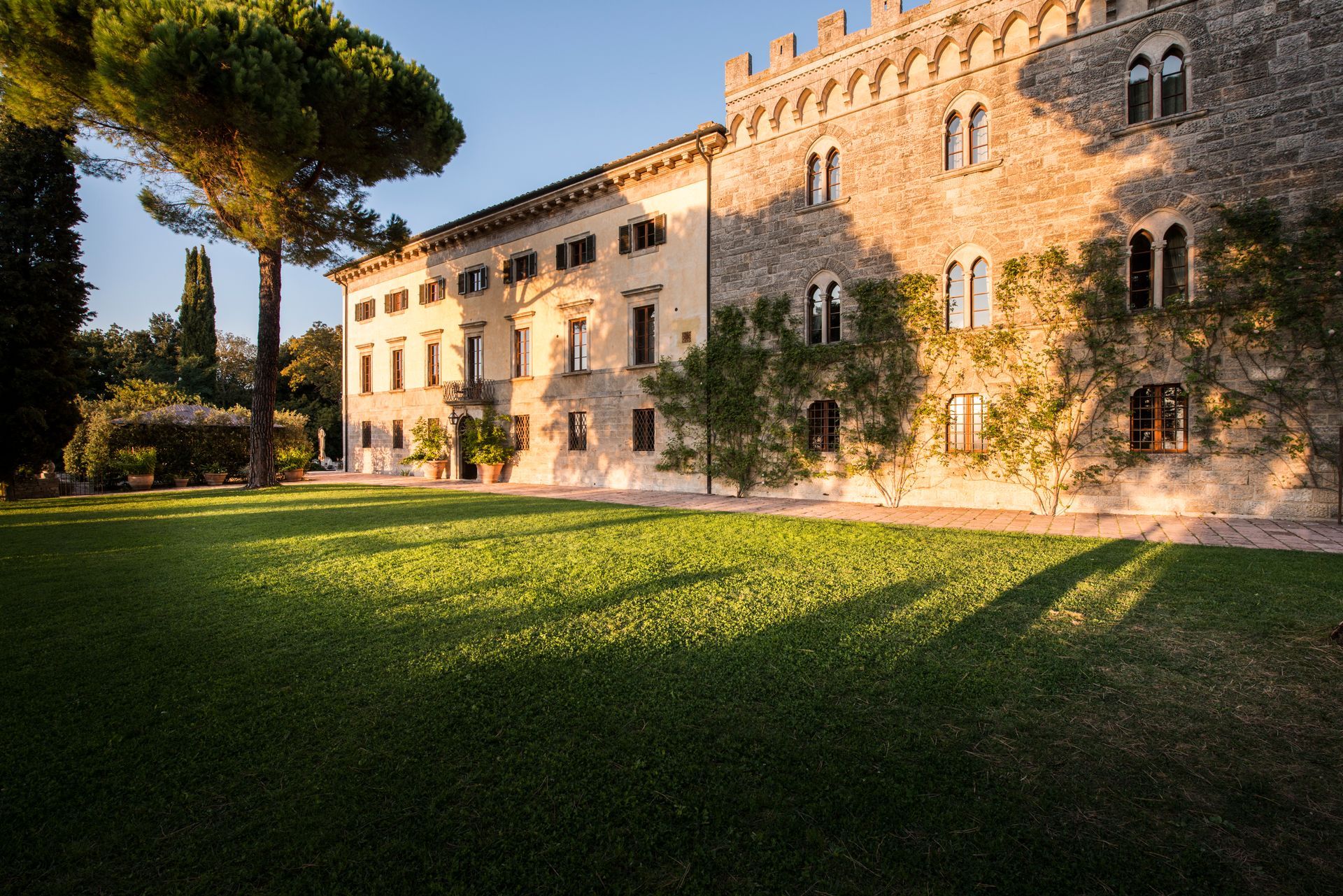 Stone castle with a lawn. The sunlight casts long shadows on the green grass.
