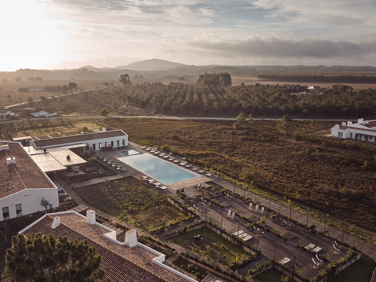 Aerial view of a white resort with a pool, surrounded by vineyards and trees, in a rural landscape.